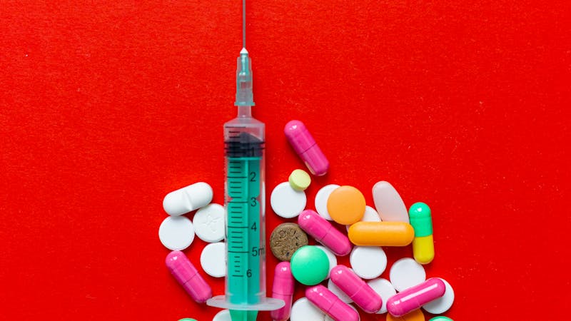 Verschiedene Tabletten, Kapseln und eine Injektionsspritze auf einem medizinischen Tablett